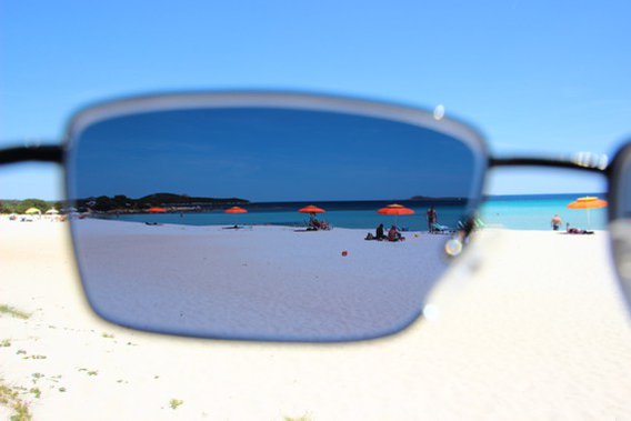 Blick durch eine Sonnenbrille auf einen Strand am Meer.